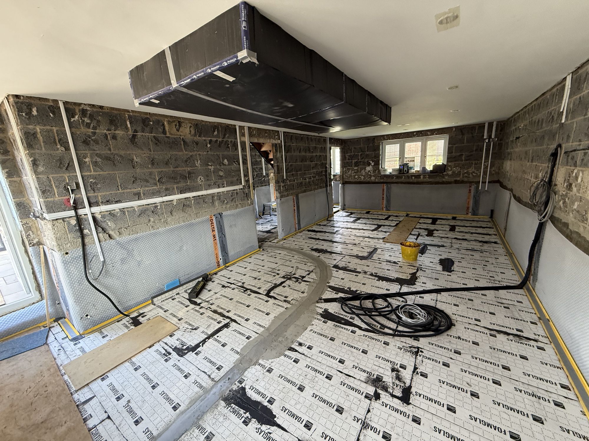 First layer of 50mm Foamglas insulation complete — water and electrical services encased within, pipework runs and conduit visible beneath the surface